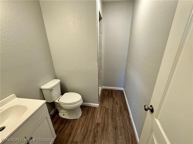 bathroom with a textured wall, toilet, vanity, wood finished floors, and baseboards