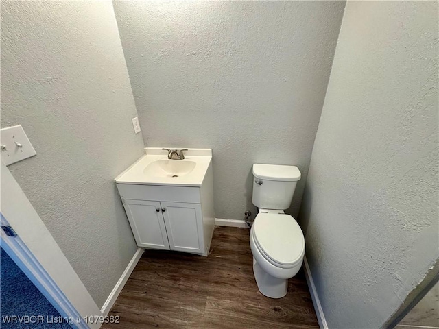 half bath featuring a textured wall, toilet, vanity, wood finished floors, and baseboards