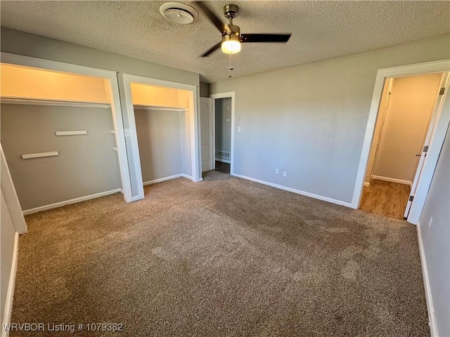 unfurnished bedroom with visible vents, baseboards, a textured ceiling, carpet floors, and two closets