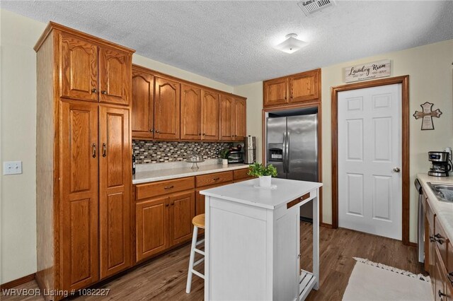 23 Wild Rose Ln, Booneville, AR 72927 - kitchen featuring stainless steel fridge with ice dispenser, a breakfast bar area, brown cabinets, dark wood-style flooring, and a textured ceiling