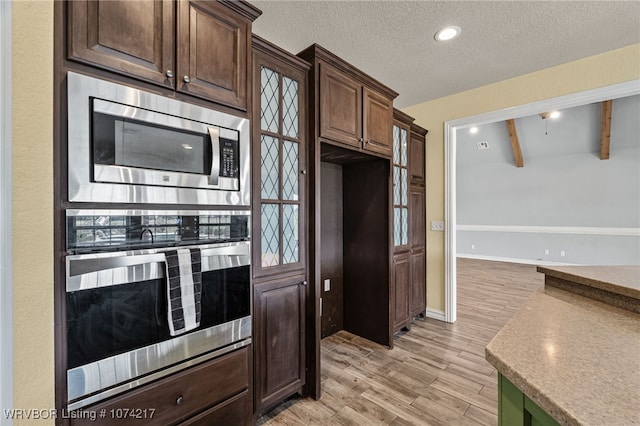 kitchen with light wood-type flooring, dark brown cabinets, a textured ceiling, vaulted ceiling with beams, and stainless steel microwave