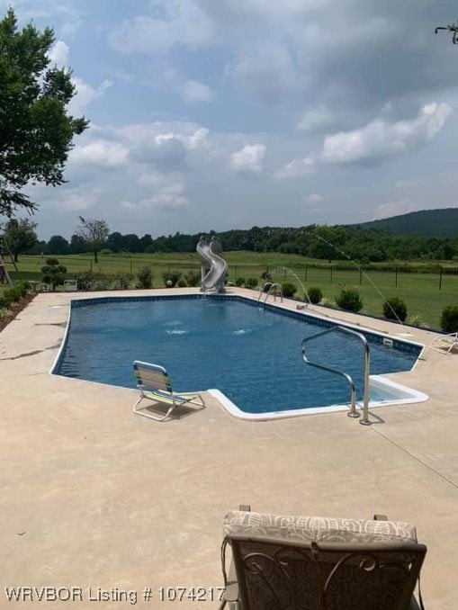 view of pool with a water slide, a rural view, and a patio