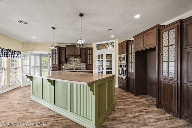 kitchen with dark brown cabinetry, french doors, pendant lighting, a center island with sink, and appliances with stainless steel finishes