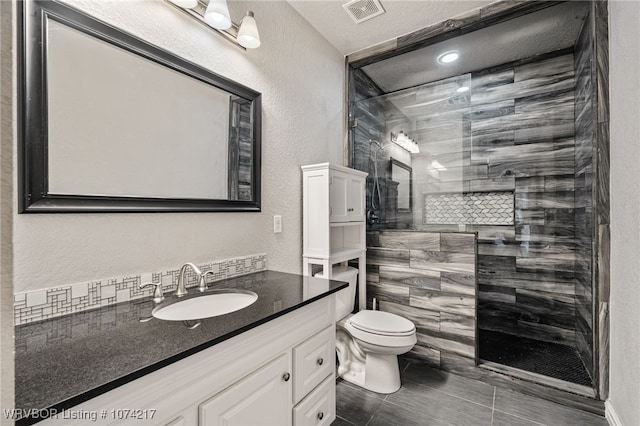 bathroom with tile patterned flooring, vanity, toilet, and tiled shower