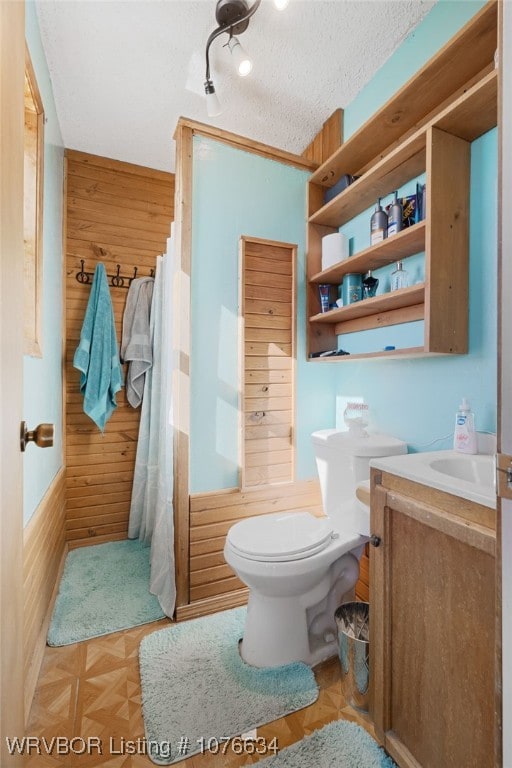 bathroom with vanity, a textured ceiling, toilet, and wooden walls