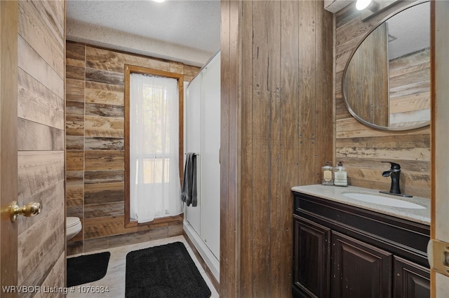 bathroom with vanity, a textured ceiling, toilet, and wood walls