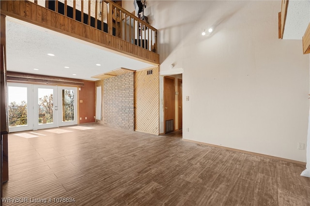 unfurnished living room featuring a high ceiling, a textured ceiling, french doors, and brick wall