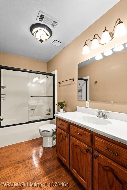 full bathroom with toilet, combined bath / shower with glass door, hardwood / wood-style flooring, and vanity