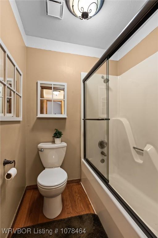 bathroom featuring hardwood / wood-style flooring, combined bath / shower with glass door, and toilet