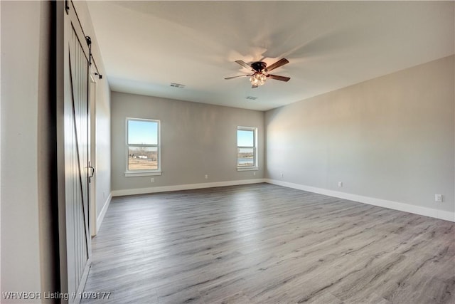 unfurnished room featuring visible vents, a barn door, a ceiling fan, light wood-style floors, and baseboards