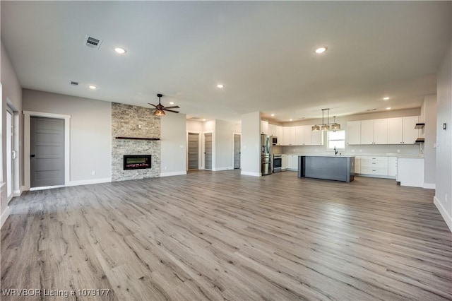 unfurnished living room with baseboards, light wood-type flooring, visible vents, and a ceiling fan