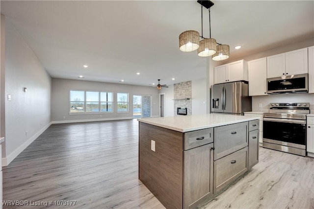 kitchen featuring stainless steel appliances, light countertops, open floor plan, white cabinets, and a kitchen island