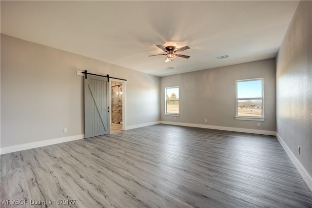 unfurnished room with a barn door, visible vents, baseboards, a ceiling fan, and wood finished floors