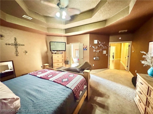 carpeted bedroom with ceiling fan, a textured ceiling, and a tray ceiling