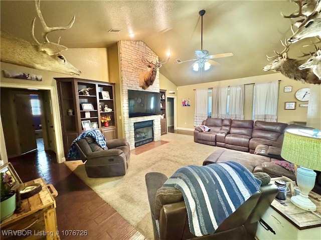 living room featuring a textured ceiling, ceiling fan, hardwood / wood-style flooring, a fireplace, and lofted ceiling