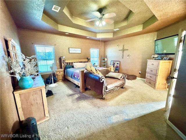 bedroom featuring ceiling fan, light colored carpet, and a tray ceiling