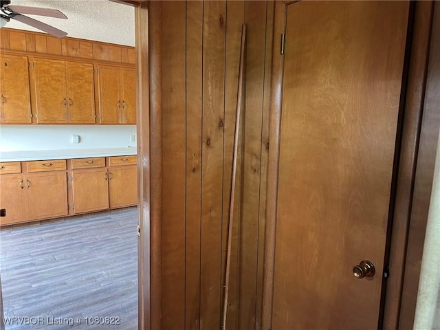 interior space with wooden walls, light countertops, a ceiling fan, and brown cabinets