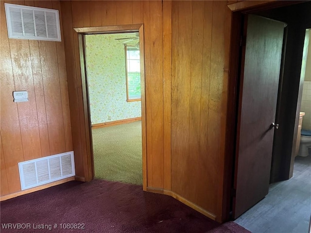 corridor with carpet, visible vents, and wood walls
