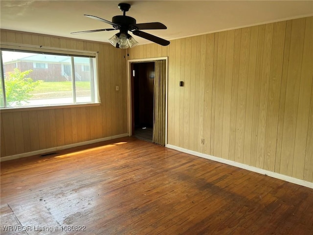 unfurnished room with ceiling fan, hardwood / wood-style flooring, baseboards, and wood walls