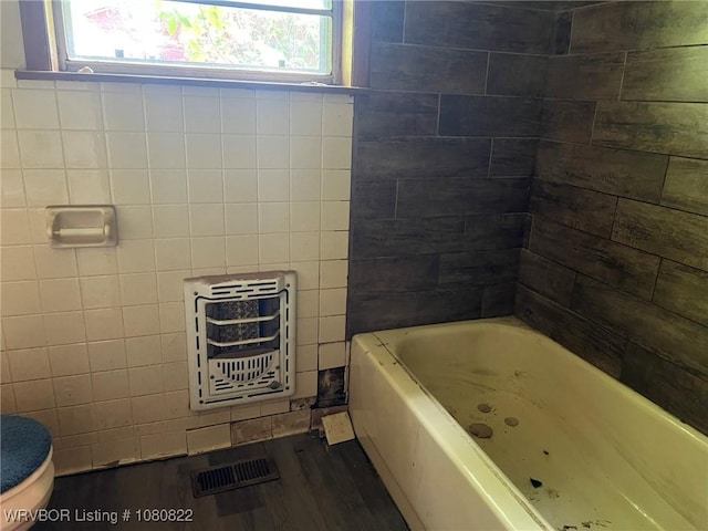 full bath with heating unit, toilet, visible vents, a tub, and wood finished floors