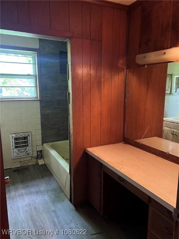 full bath with heating unit, a bath, and wooden walls