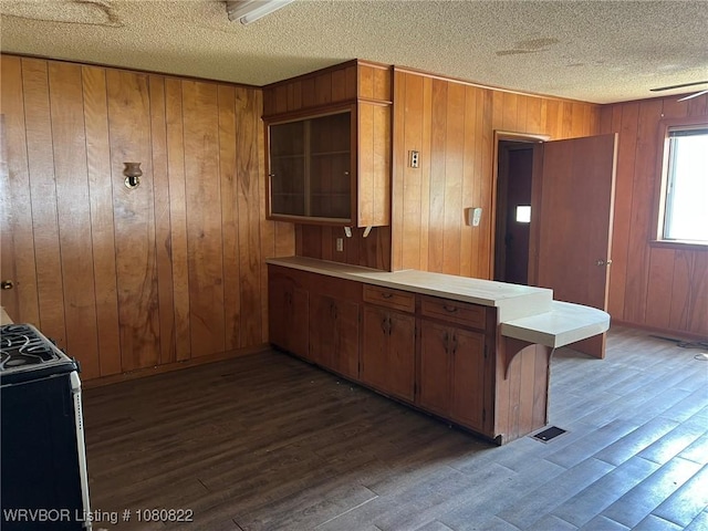 kitchen featuring a textured ceiling, gas range oven, a peninsula, brown cabinets, and light countertops