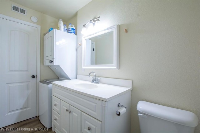 bathroom with visible vents, toilet, wood finished floors, vanity, and stacked washing maching and dryer