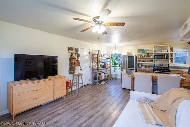 living room with ceiling fan with notable chandelier, visible vents, and wood finished floors