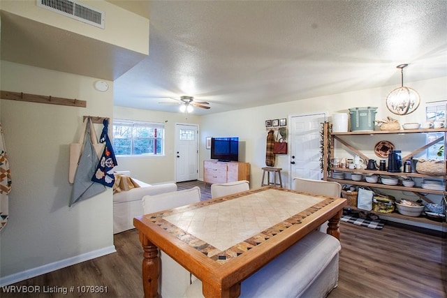 dining room with a textured ceiling, ceiling fan with notable chandelier, wood finished floors, visible vents, and baseboards