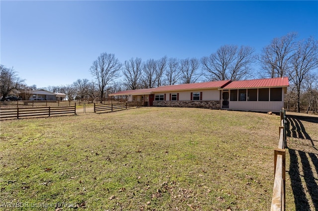 view of front of home with a front yard, a sunroom, metal roof, fence, and stone siding