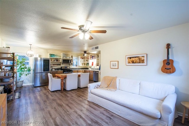 living area with dark wood-style flooring, visible vents, ceiling fan, and a textured ceiling