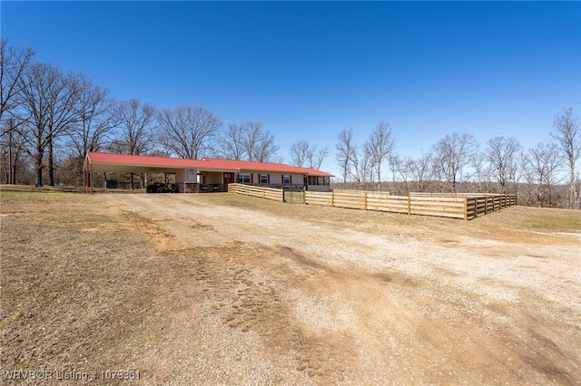 exterior space with a rural view, an outdoor structure, dirt driveway, a carport, and an exterior structure