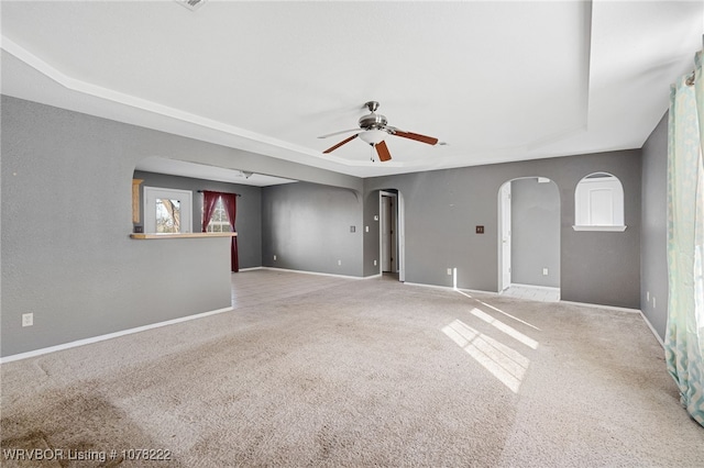 carpeted spare room featuring a tray ceiling, ceiling fan, and a healthy amount of sunlight