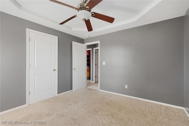 unfurnished bedroom featuring a tray ceiling, ceiling fan, and light colored carpet