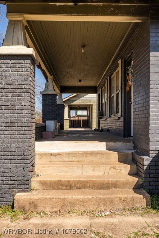 doorway to property with brick siding, covered porch, and driveway