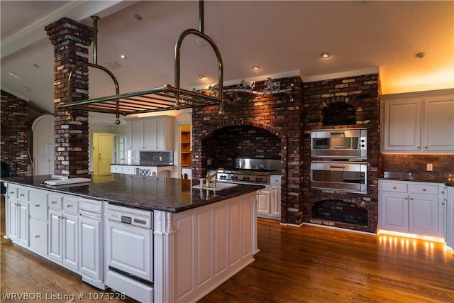 kitchen with white cabinets, stainless steel microwave, oven, and a kitchen island with sink