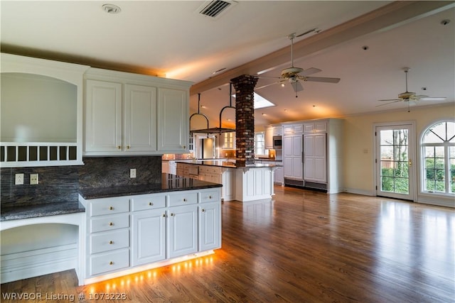 kitchen with dark stone countertops, tasteful backsplash, a kitchen island, white cabinetry, and decorative columns