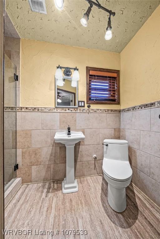 full bath with visible vents, a stall shower, toilet, and tile walls