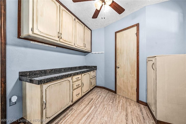 kitchen with a textured ceiling, dark countertops, light wood finished floors, baseboards, and ceiling fan