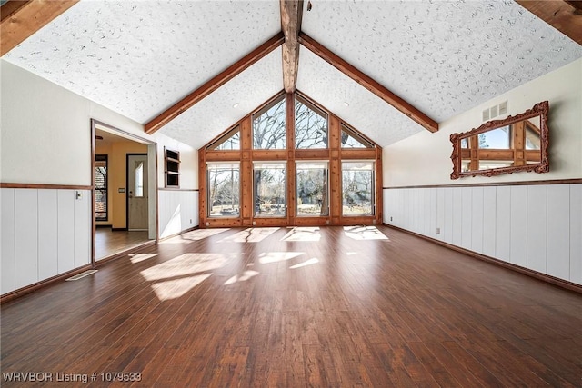 unfurnished living room with visible vents, beam ceiling, high vaulted ceiling, hardwood / wood-style flooring, and wainscoting