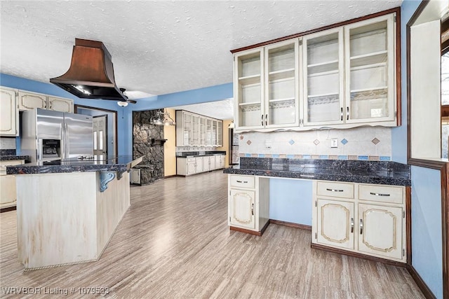 kitchen featuring glass insert cabinets, tasteful backsplash, light wood-style flooring, and stainless steel fridge with ice dispenser