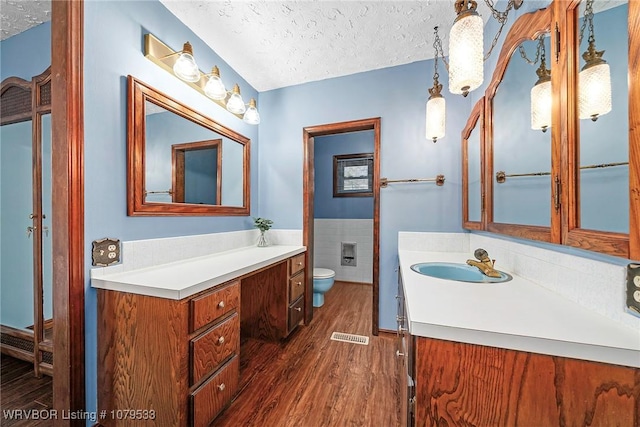 bathroom featuring toilet, a textured ceiling, wood finished floors, tile walls, and vanity