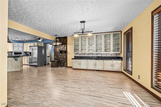 kitchen with light wood-style flooring, dark countertops, a textured ceiling, appliances with stainless steel finishes, and glass insert cabinets