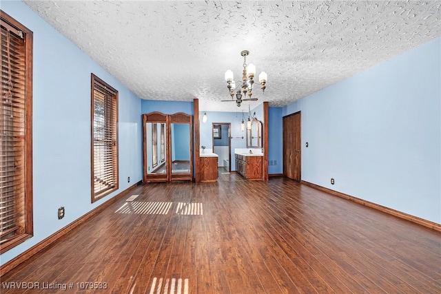 interior space with dark wood finished floors, a chandelier, a textured ceiling, and baseboards