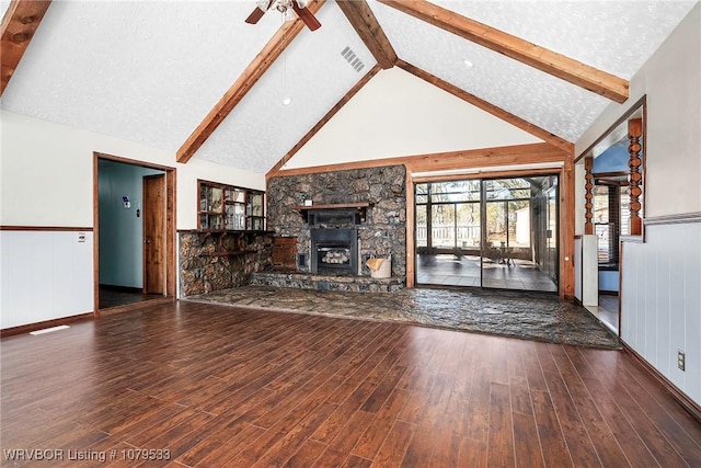 unfurnished living room featuring wood finished floors, visible vents, a fireplace, wainscoting, and beamed ceiling