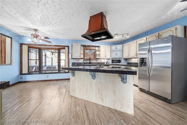 kitchen featuring island exhaust hood, light wood-style floors, appliances with stainless steel finishes, a textured ceiling, and a kitchen bar