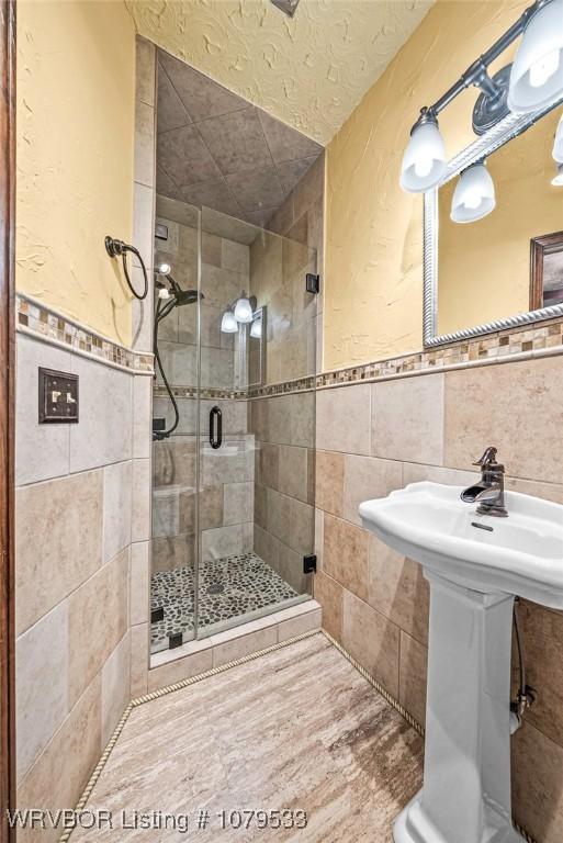 bathroom featuring a wainscoted wall, tile walls, and a stall shower