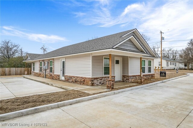 view of front of property featuring driveway, roof with shingles, fence, and brick siding