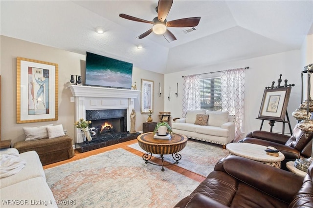 living room with a tray ceiling, vaulted ceiling, ceiling fan, wood-type flooring, and a premium fireplace