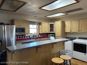 kitchen with light wood finished floors, stainless steel appliances, glass insert cabinets, a kitchen bar, and washer and clothes dryer